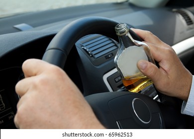 Driver with a bottle of alcohol sits behind the steering wheel