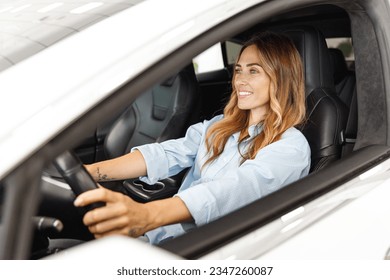Driver calm woman customer buyer client in shirt hold put hands on steering wheel choose auto want buy new automobile in car showroom vehicle salon dealership store motor show indoor. Sales concept.