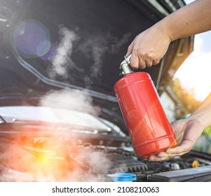 The driver of the car directs a powder fire extinguisher at the engine compartment of the car in which there is fire and smoke. Car fire, background