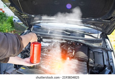 The Driver Of The Car Directs A Powder Fire Extinguisher At The Engine Compartment Of The Car In Which There Is Fire And Smoke. Car Fire, Background. Electrical Short Circuit