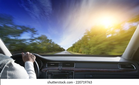 Driver in car holding steering wheel. Blurred road and sky 