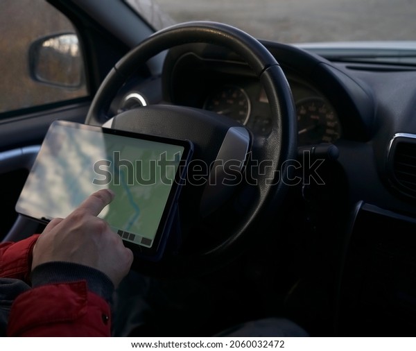 driver of\
the car installs a tablet computer on the front panel as a car\
Navigator. male hand holding black tablet with isolated screen,\
steering wheel in background. Mockup. no\
face.