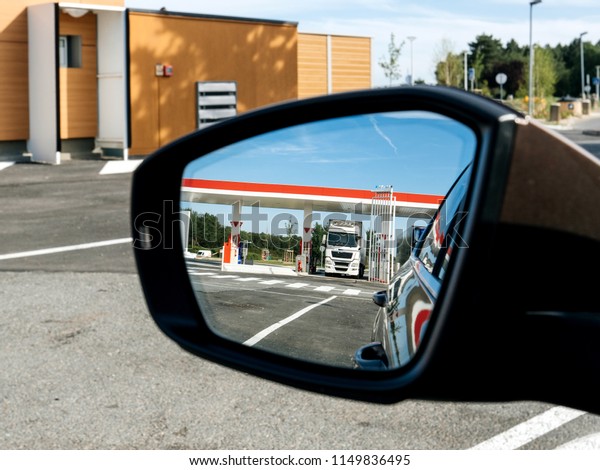 Driver car rear view mirror with\
reflection of white truck filling gas at the gas\
station