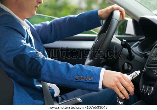 the driver of the car sits behind\
the wheel and holds in his hand an electronic\
cigarette
