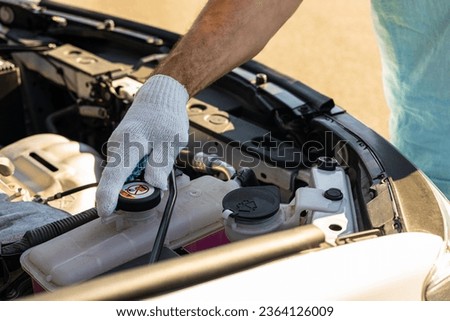 driver check the coolant level in the engine compartment of the car. car coolant expansion tank. master inspects the engine compartment of the car. car engine coolant level