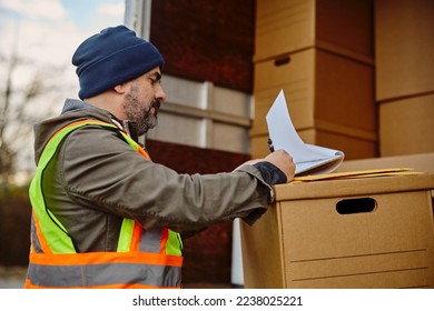Driver checking shipment list while checking packages in back of a truck.