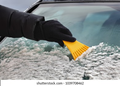 Driver Cleaning Snow From Windshield Of Car Using Scraper