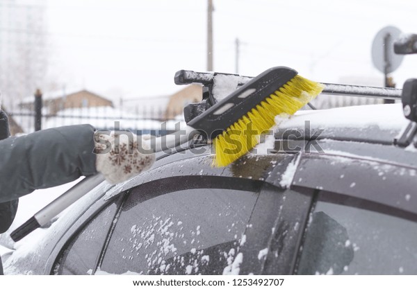 The driver cleans the car from the snow with a\
brush on the winter street.