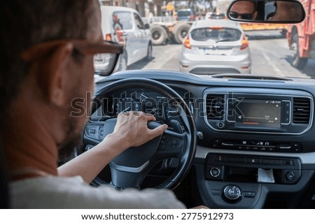 A driver concentrates on the road while navigating through heavy traffic in a bustling city during midday, surrounded by various vehicles.