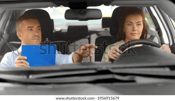 driver courses, exam and\
people concept - young woman and driving school instructor with\
clipboard in car