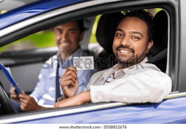 driver courses, exam and people concept - happy\
smiling indian young man with license and driving school instructor\
with clipboard in car