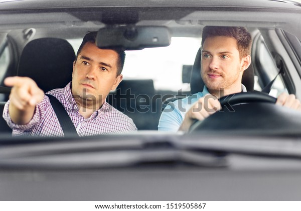 driver courses and people concept -\
car driving school instructor teaching young man to\
drive