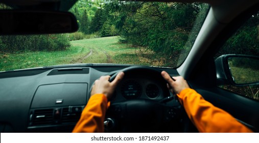 Driver dressed bright orange jacket driving a modern off road right hand drive RHD car on the mountain green forest country road. POV inside car windscreen view point. Safely auto driving concept.