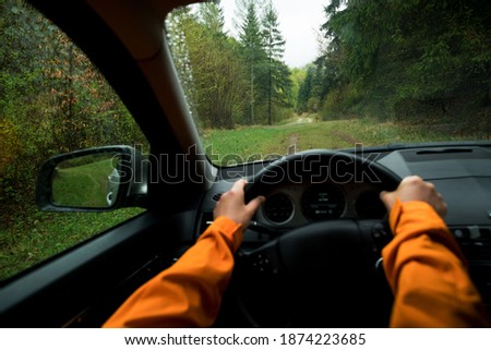 Driver dressed bright orange jacket driving a modern off road left hand drive LHD car on the mountain green forest country road. POV inside car windshield view point. Safely auto driving concept.