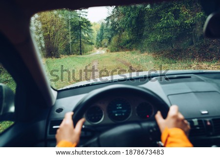 Driver dressed bright orange jacket driving a modern off road left hand drive LHD car on the mountain green forest country road. POV inside car windshield view point. Safely auto driving concept.