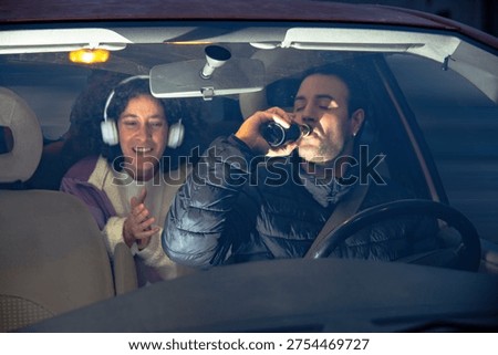 Driver drinking beer while passenger looking on happily