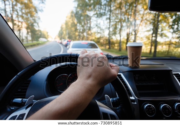 The driver is drinking coffee
behind the wheel closeup. Transportation, drinks, people and
vehicle concept - close up of man drinking coffee while driving
car