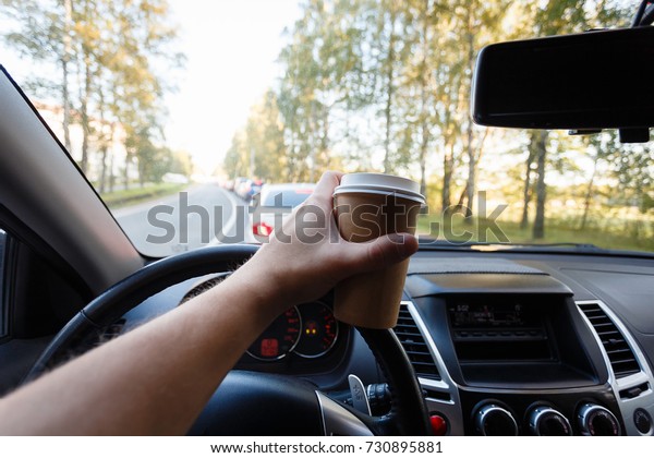 The driver is drinking coffee
behind the wheel closeup. Transportation, drinks, people and
vehicle concept - close up of man drinking coffee while driving
car
