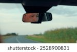 Driver drives car, happy emotions. Weekend, car, road, sports. Male driver in reflection of rear view mirror. Serious man travels by car, looks at road, drives car. Auto movement on road outside city