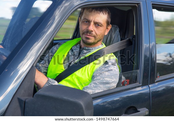 Driver driving a car in a signal vest and with a\
seat belt.