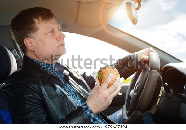 The driver eats at the wheel of the car without\
taking his eyes off the\
road.