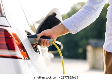 The driver of the electric car inserts the electrical connector to charge the batteries. Unrecognizable man attaching power cable to electric car. Electric vehicle Recharging battery charging port.