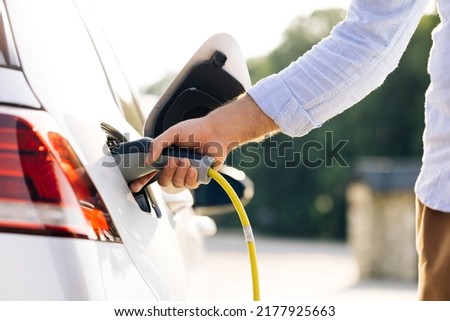 The driver of the electric car inserts the electrical connector to charge the batteries. Unrecognizable man attaching power cable to electric car. Electric vehicle Recharging battery charging port. Stockfoto © 