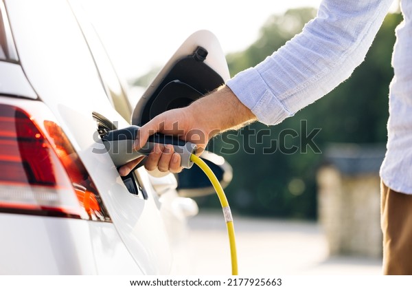 The driver of the electric car inserts the\
electrical connector to charge the batteries. Unrecognizable man\
attaching power cable to electric car. Electric vehicle Recharging\
battery charging port.