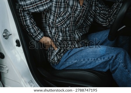 Driver experiencing lower back pain while sitting in a car, representing poor posture, musculoskeletal discomfort, driving fatigue, health issues, and ergonomic concerns.