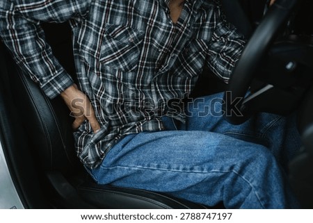 Driver experiencing lower back pain while sitting in a car, representing poor posture, musculoskeletal discomfort, driving fatigue, health issues, and ergonomic concerns.