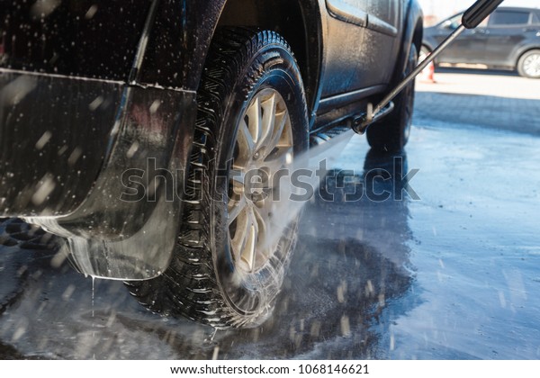 The driver, the girl washes her\
SUV in the stall car wash using a jet of high pressure water with\
soap. Car wash with their own hands. Self-service car\
wash.