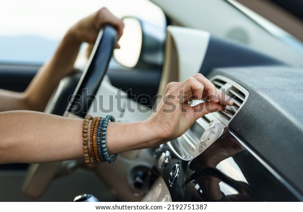 Driver goes on road trip sitting at steering wheel\
and driving in rural area on hot summer day. Woman puts hand on\
modern panel vent to check cold air flow and operation of\
ventilation system