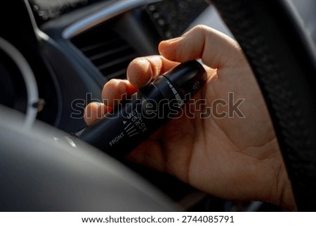 Driver hand adjusting windshield wiper control lever on steering column inside car interior, selecting mist and interval modes.