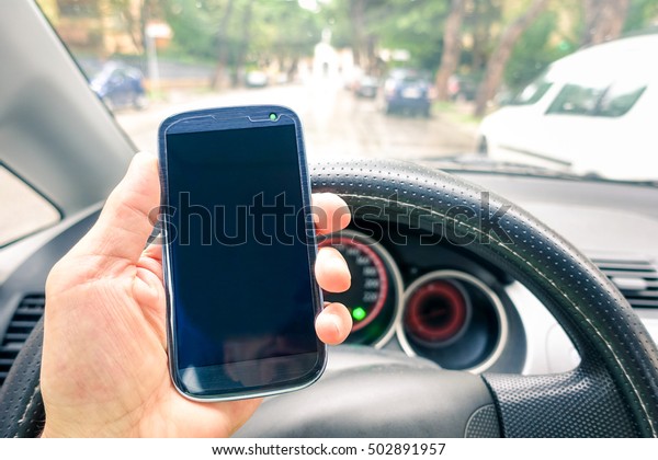 Driver hand holding mobile phone inside car on the\
road - Close up of smartphone with empty screen to add text or\
message - Modern concept of dangerous human habits on transport\
vehicle in daily life