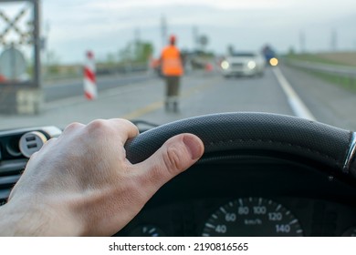 Driver Hand Is On The Steering Wheel, Which Stands And Passes Oncoming Cars At The Command Of A Traffic Controller, Builder At The Time Of Repair Of The Highway, Bridge