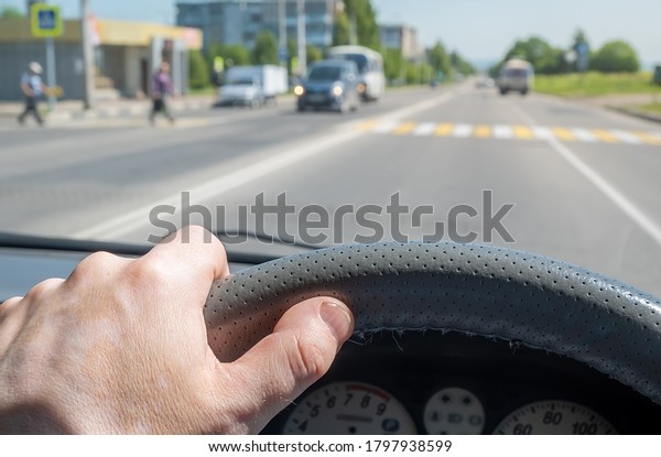 the driver hand on the\
steering wheel of a car approaching a pedestrian crossing where\
pedestrians