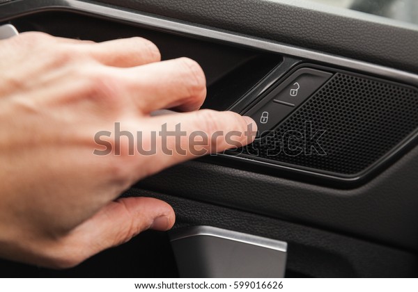 Driver hand pushes door\
lockers button of luxury crossover car. Close up photo with\
selective focus