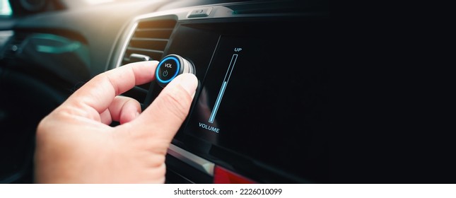 The driver hand is turning up or down the volume of the car music player or radio, panoramic banner with copy space on black background