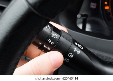 Driver hand turning on headlight using under steering switch; Headlight switch; Turn signal lever; Fog light switch; Close-up view;