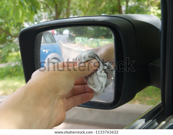 A driver hand wiping a car side mirror, outdoor\
cropped closeup