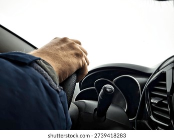 Driver handles the steering wheel while navigating a snowy road during winter commute, focused on transportation safety.