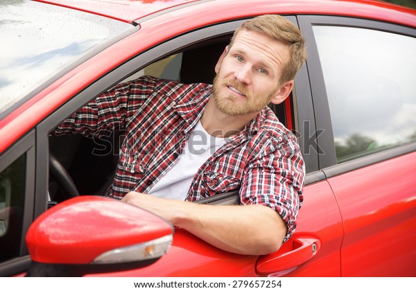 Driver.\
Happy smiling man in new red car on the\
road.