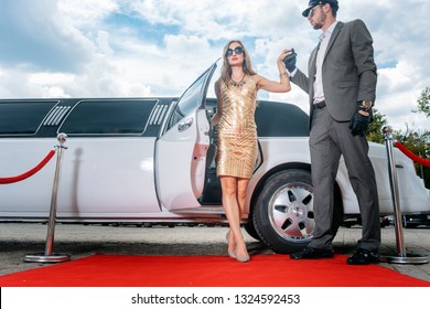 Driver helping VIP woman or star out of limo on red carpet to a reception