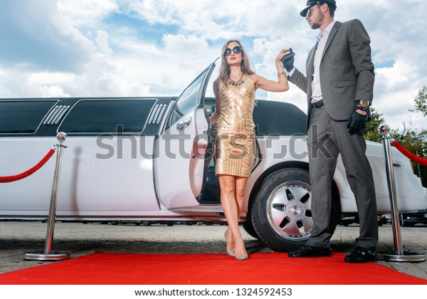 Driver helping VIP woman or star out of limo on red\
carpet to a reception 