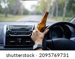 A driver holding alcoholic bottle while driving. Drunk driving concept.