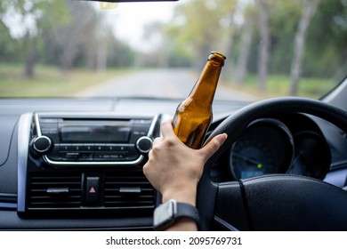 A driver holding alcoholic bottle while driving. Drunk driving concept.
