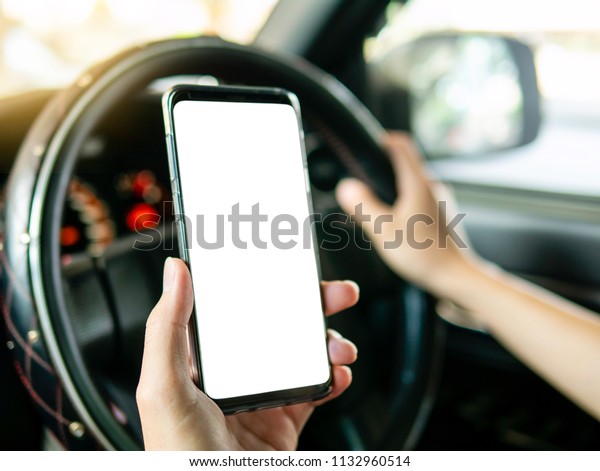 Driver\
holding smartphone in hand, use smart phone while driving. Isolated\
white screen for mock up, graphic design or app promotion. Steering\
wheel interior right-hand drive car in\
background.