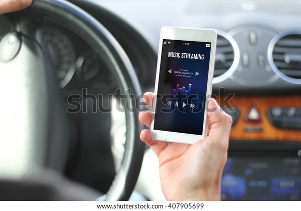 driver holding smartphone with\
music streaming interface. All screen graphics are made\
up.