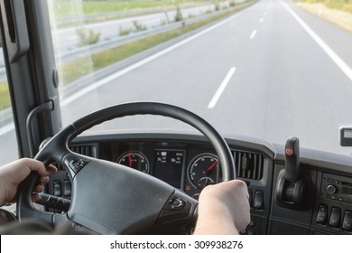 The Driver Is Holding The Steering Wheel And Is Driving A Truck On The Empty Highway. Focused On The Wheel And Drivers Hand.