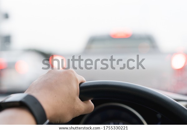 Driver holding a steering wheel on\
the top (12 O\'Clock position) while driving a car on heavy traffic\
road. Asian driver driving a vehicle on highway close\
up.